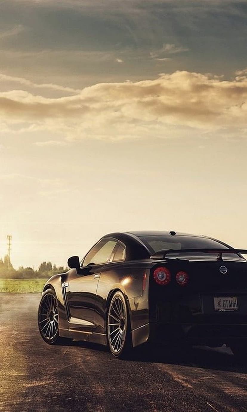 Black Nissan GT-R rear showing round taillights and spoiler on an asphalt road during a cloudy golden sunset.