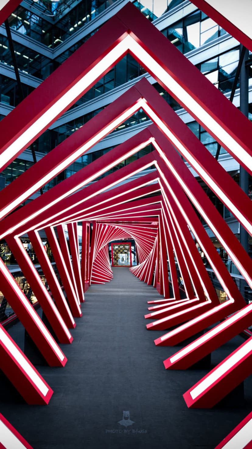 Repeating red square frames with white glowing borders create a deep architectural tunnel leading to a bright exit.