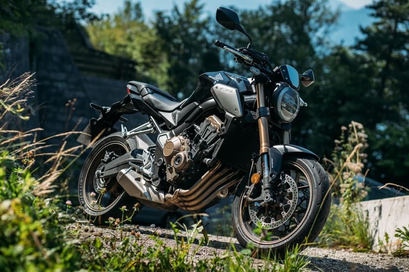 Honda CB650R motorcycle with bronze forks and engine details parked on a sunlit gravel path near green trees.