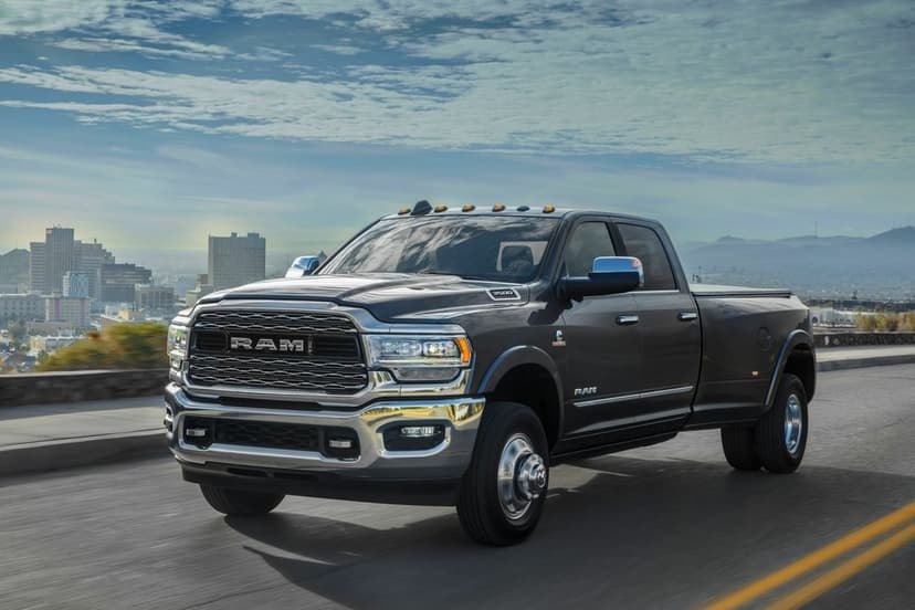 Dark gray RAM 3500 dually truck driving on a road with a city skyline and distant mountains under a blue sky.