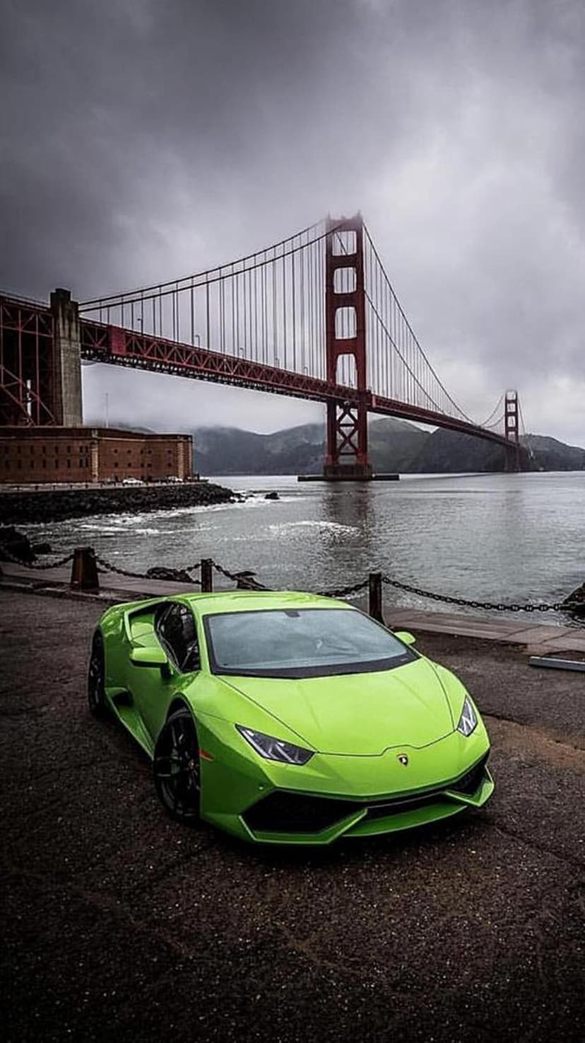 Lime green Lamborghini parked on asphalt with the red Golden Gate Bridge and misty San Francisco sky behind it.