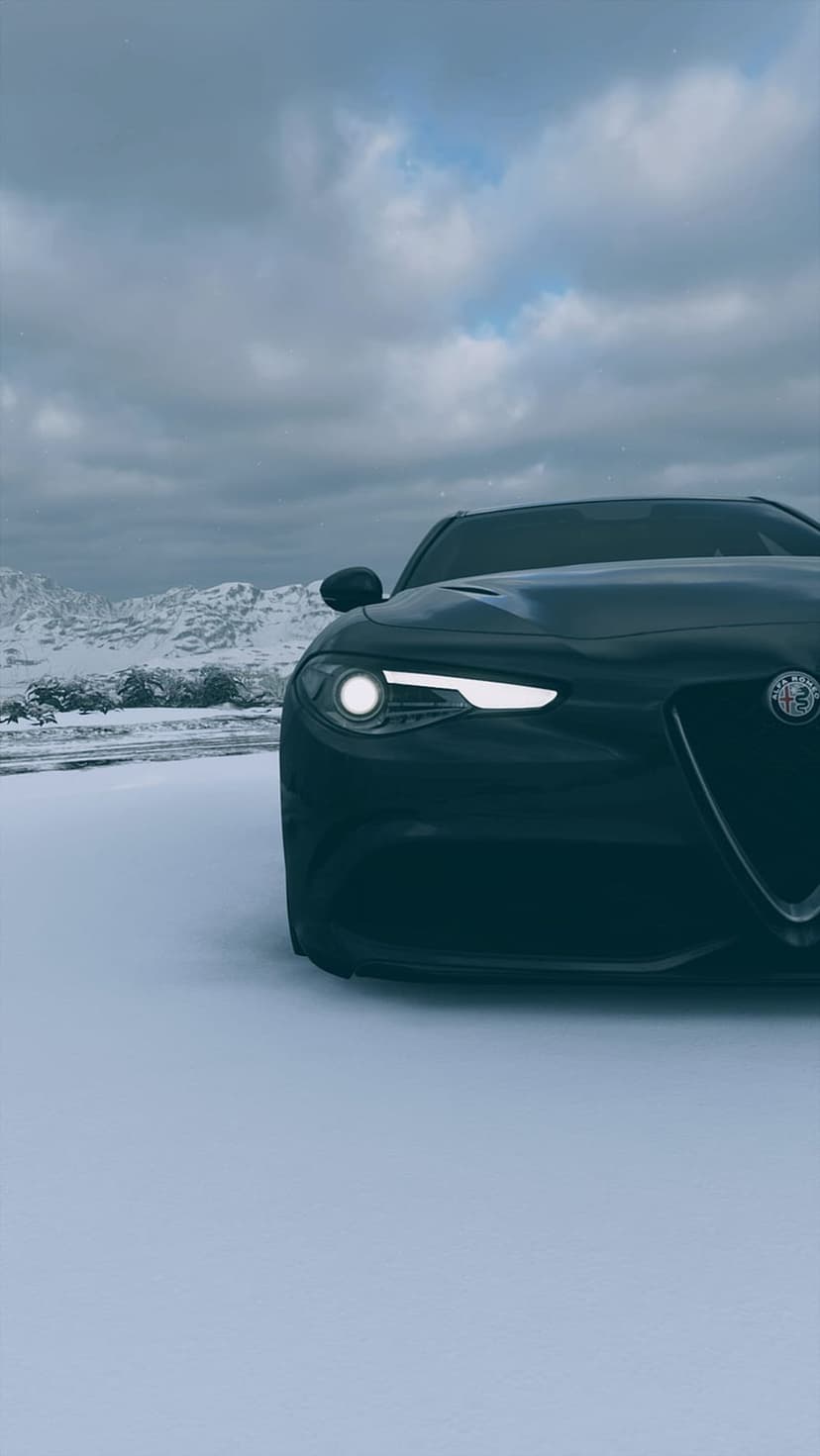 Black sports sedan with glowing headlights parked on a snowy ground before a range of jagged winter mountains.