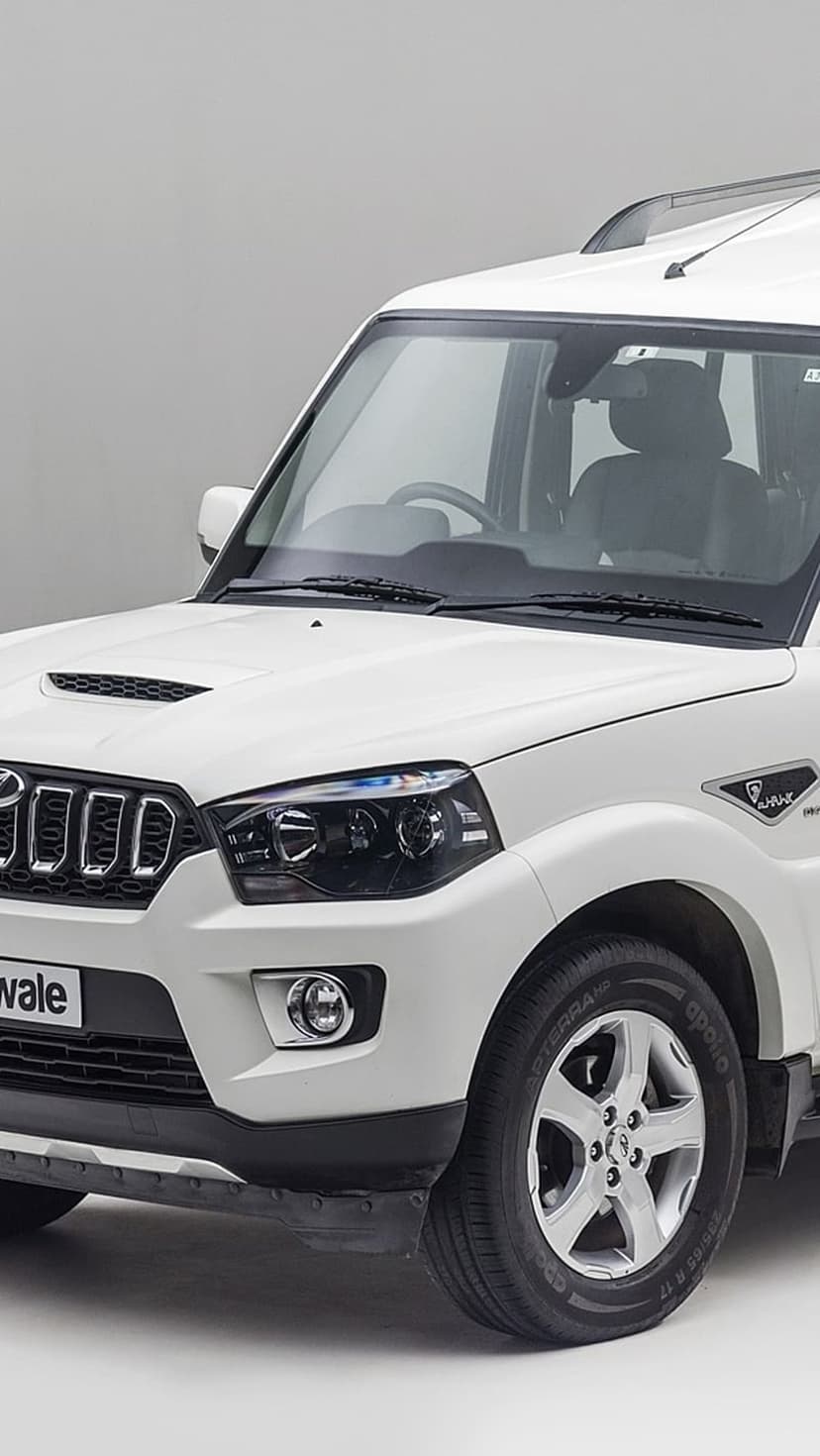 White Mahindra Scorpio S11 SUV front view with chrome grille and projector lights against a grey background.
