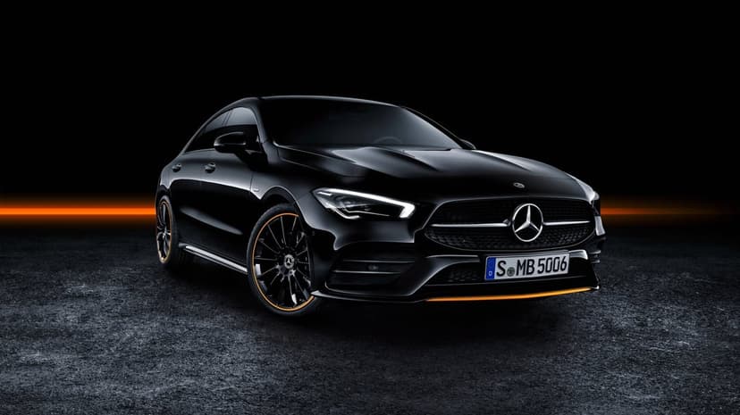 Black Mercedes-Benz CLA coupe with orange wheel accents parked on dark asphalt under dramatic studio lighting.