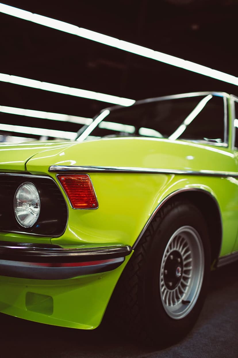 Lime green classic car fender featuring a chrome trim line, round headlight, and a polished retro alloy wheel.