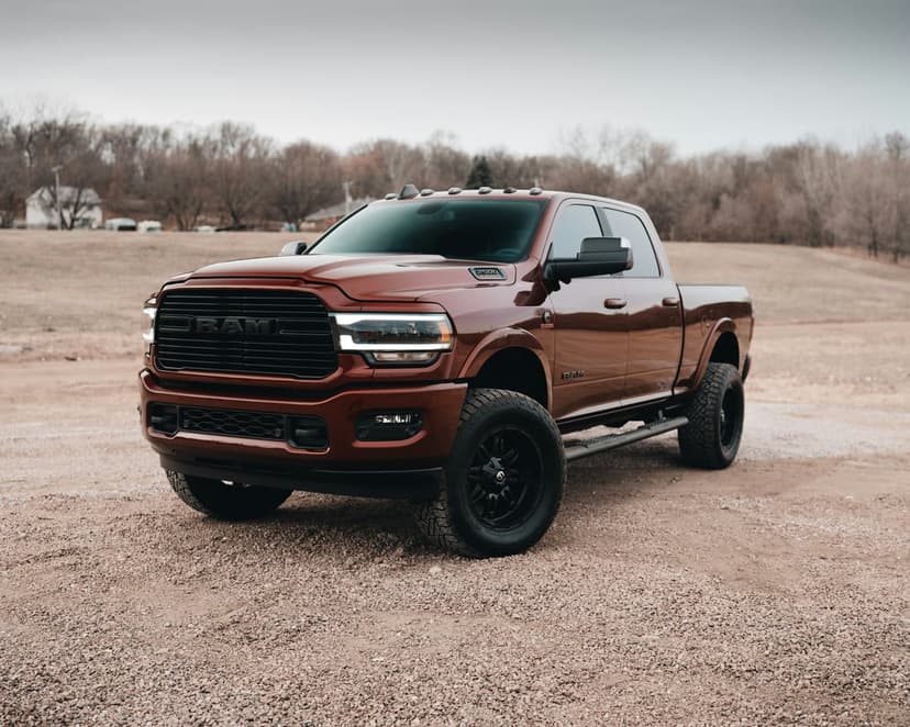 Dark red Ram 3500 truck with custom black wheels and lifted suspension parked on gravel against a cloudy sky.