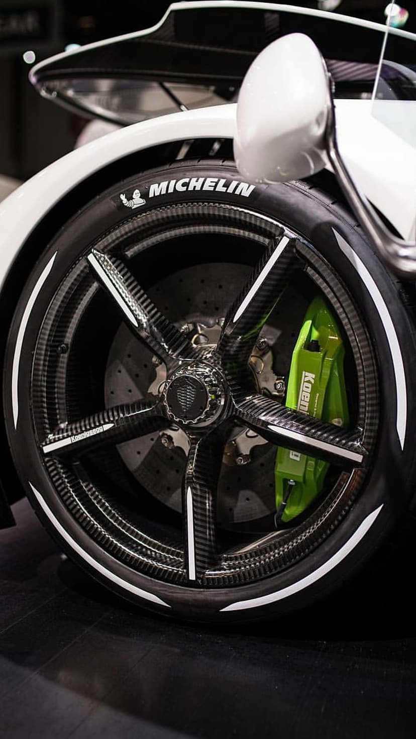 Koenigsegg carbon fiber wheel rim with a bright green brake caliper and white Michelin tire lettering close-up.