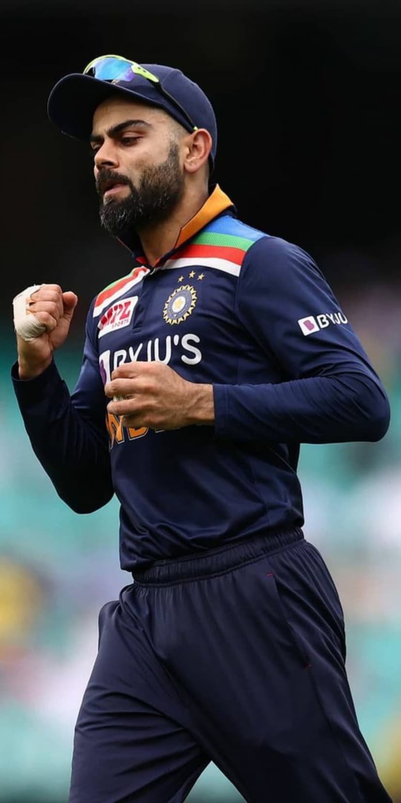 Virat Kohli raises a clenched fist while wearing a navy blue Indian cricket jersey with the official BCCI emblem.