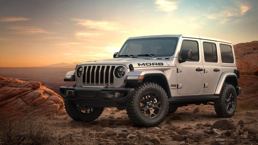 Silver Jeep Wrangler Moab Edition on rocky desert ground with a golden sunset sky and red rock background.