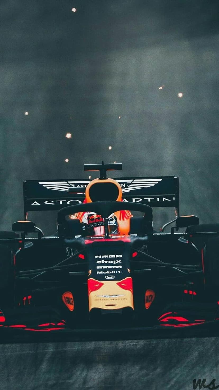 Formula 1 racing car with a driver in an orange helmet trailing bright sparks on a dark asphalt track.