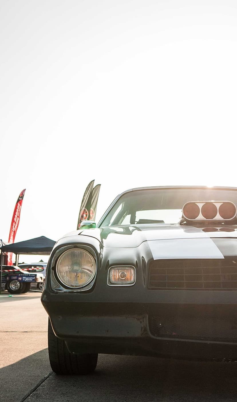 Black vintage Chevrolet Camaro with a white racing stripe and hood scoop parked outdoors at a low-angle view.