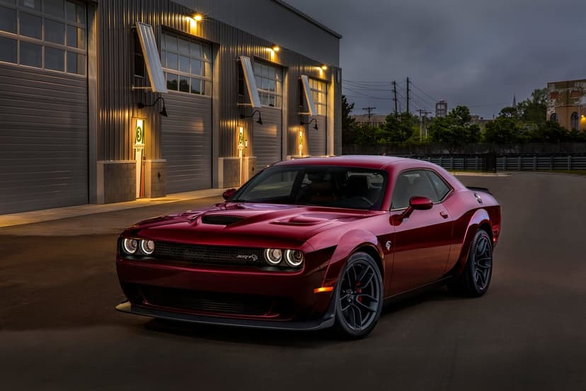 Red Dodge Challenger SRT Hellcat Widebody parked in front of a modern garage with warm exterior lighting at dusk.