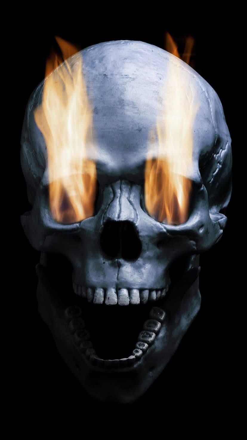 Weathered metallic skull with glowing orange flames in eye sockets and an open mouth on a black backdrop.