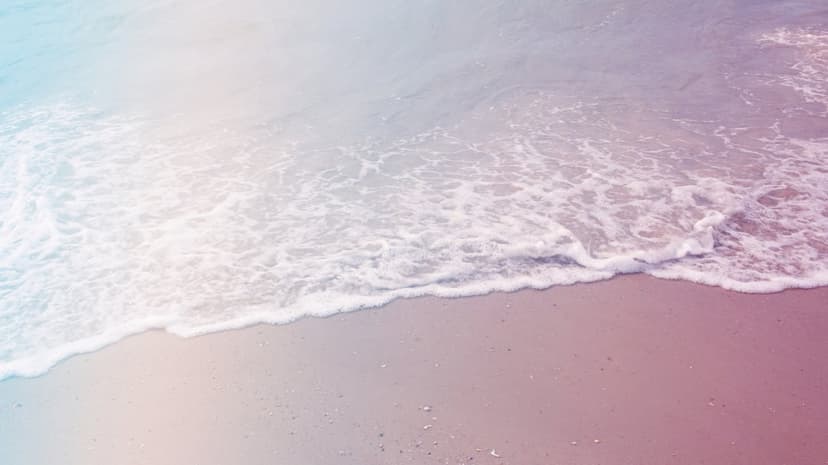 Pastel sea foam glides across a pale sandy beach during a soft sunset, creating a tranquil coastal scene.