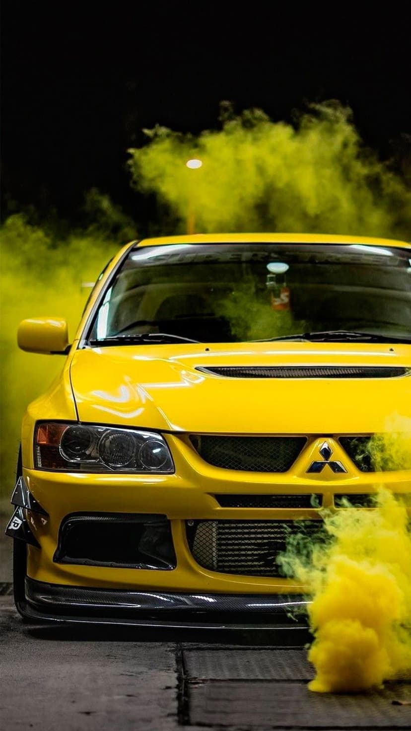 Yellow Mitsubishi Lancer Evolution with carbon fiber canards surrounded by yellow smoke on a dark background.