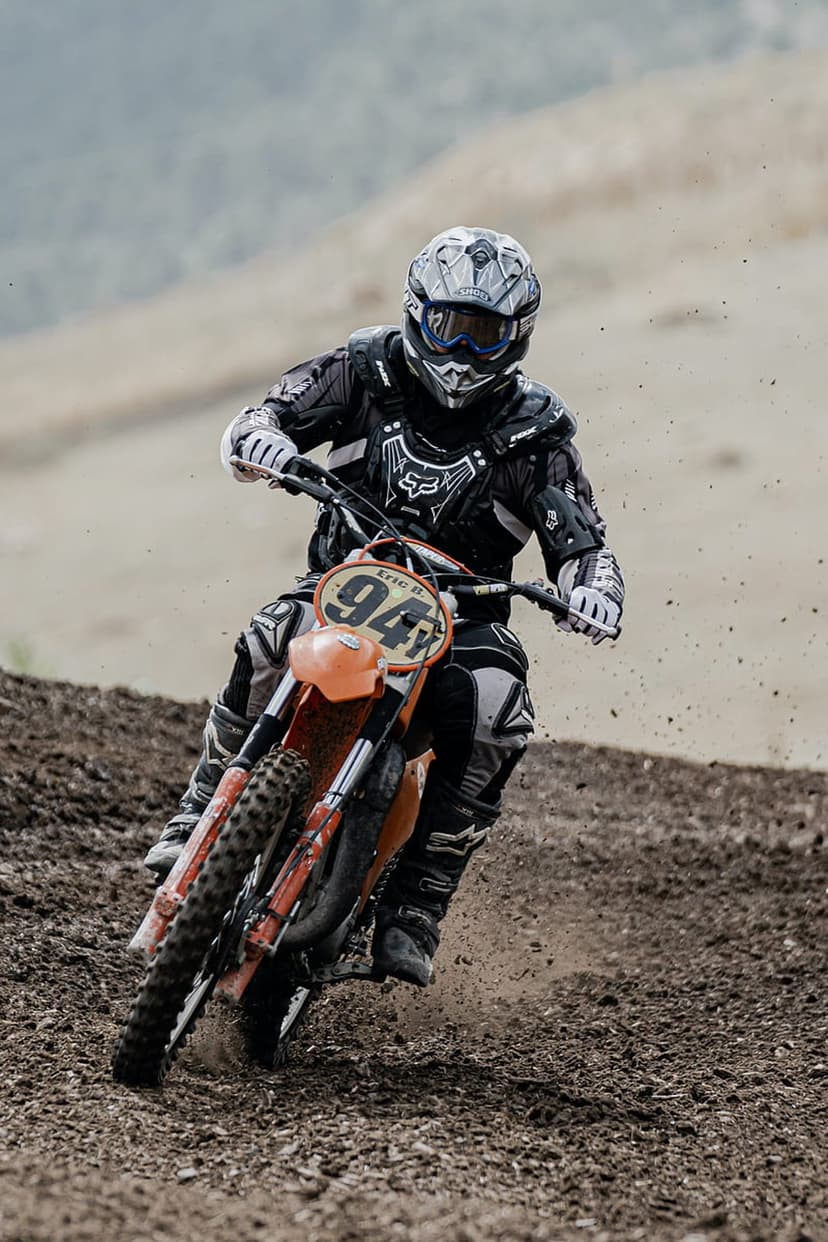 Motocross rider on an orange dirt bike labeled 94 kicks up dust while racing through a sharp off-road track curve.