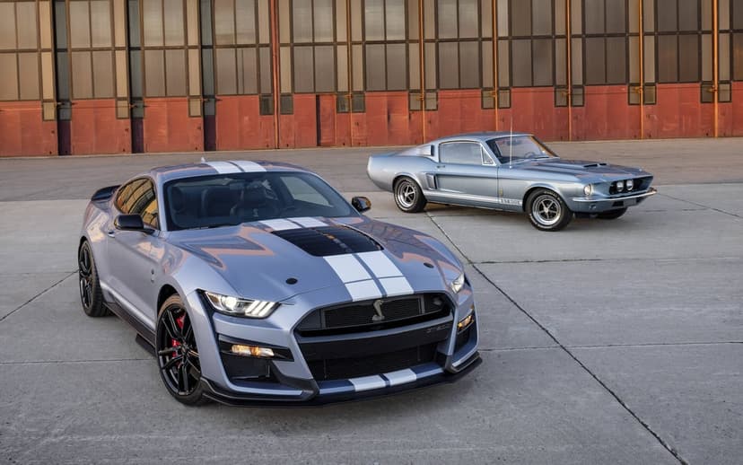 Modern and classic Shelby GT500 Mustangs in metallic blue with white stripes parked on a wide concrete airfield.