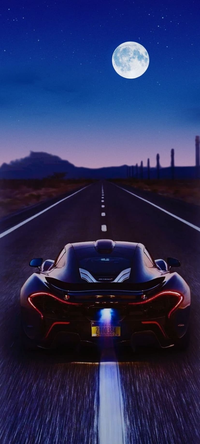 Black supercar with red taillights speeds along a desert highway under a bright full moon and starry night sky.