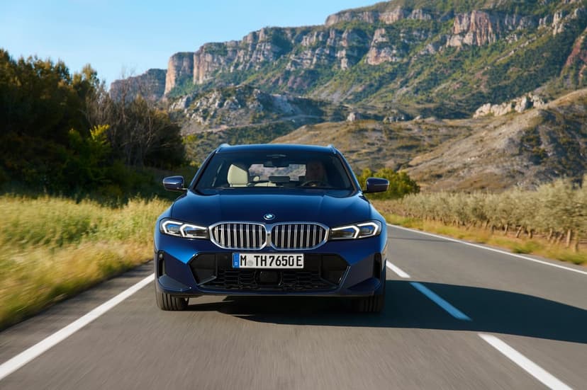 Blue BMW station wagon driving on a paved road with blurred motion and massive rocky mountains in the distance.