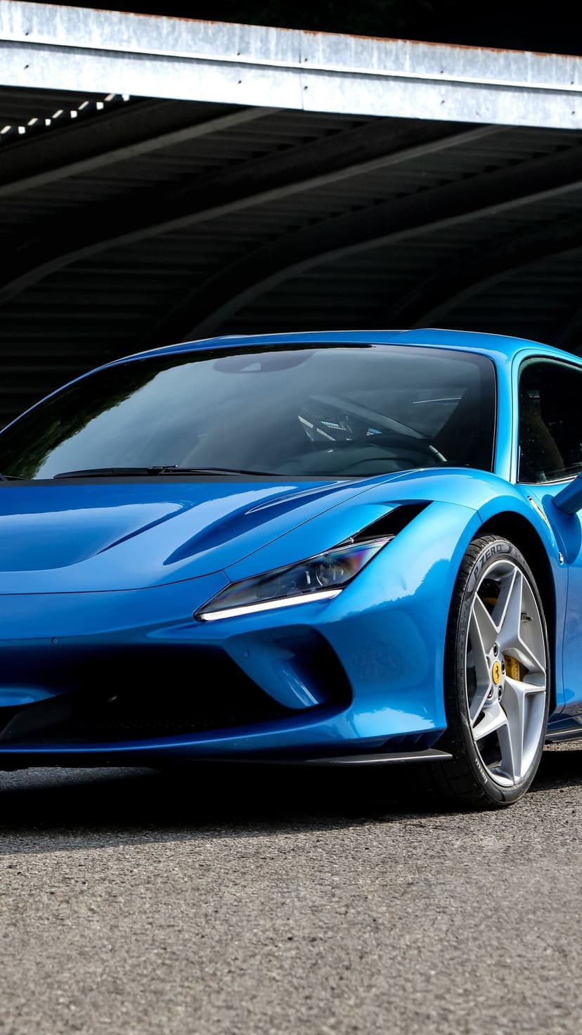 Blue Ferrari F8 Tributo supercar with LED headlights and silver alloy wheels parked under a dark overhang.