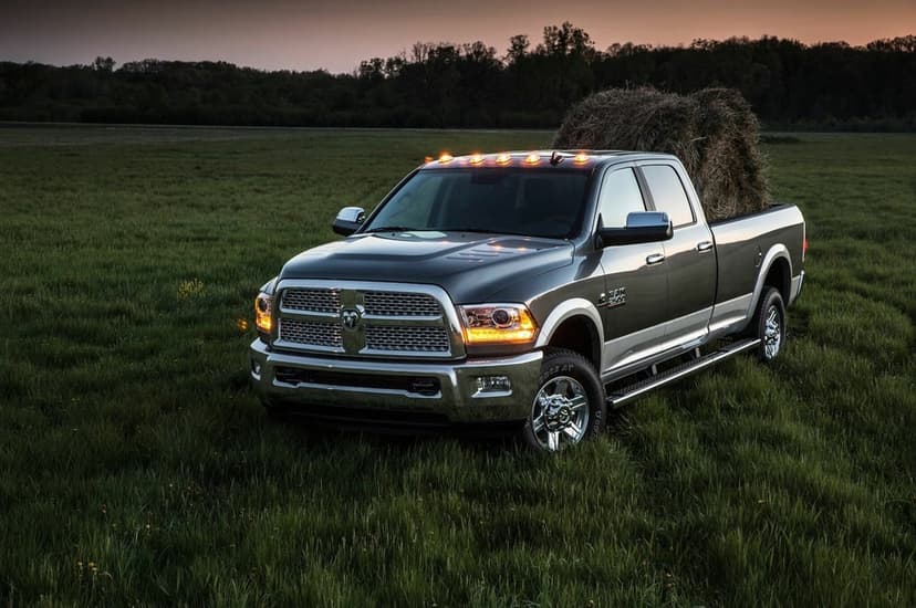 Metallic RAM 2500 pickup truck with a large hay bale in a green pasture at sunset with glowing amber lights.