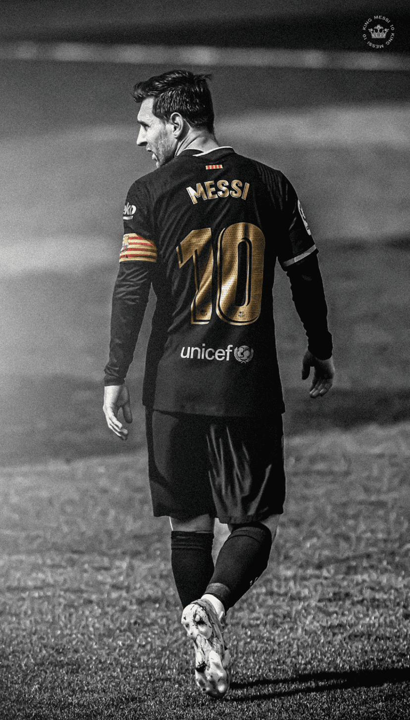 Lionel Messi seen from behind wearing a black and gold Barcelona jersey while standing on a grayscale pitch.