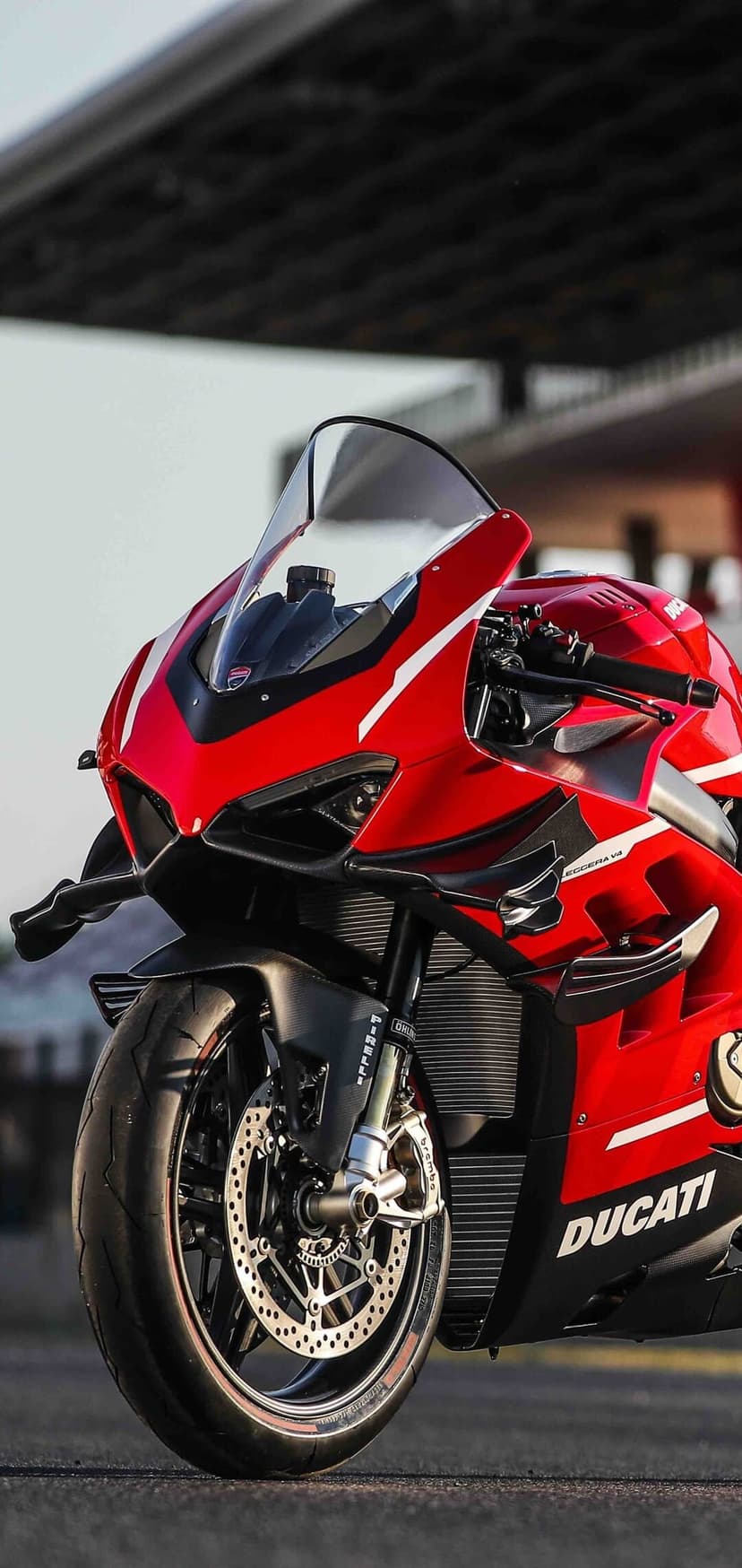 Red Ducati Superleggera V4 motorcycle featuring carbon fiber winglets and Brembo brakes in a blurred track setting.