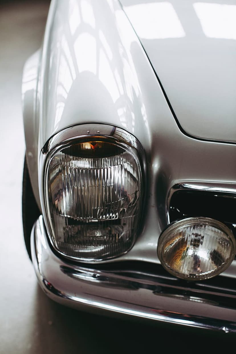 Silver vintage car headlight with ribbed glass and a reflective chrome bumper in a vertical close-up shot.