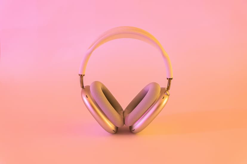 Silver over-ear headphones centered on a soft pink and orange gradient background with subtle metallic highlights.