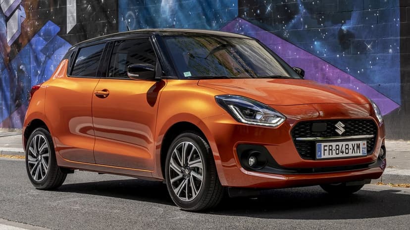 Metallic orange Suzuki Swift parked on an urban street in front of a colorful purple and blue cosmic graffiti mural.