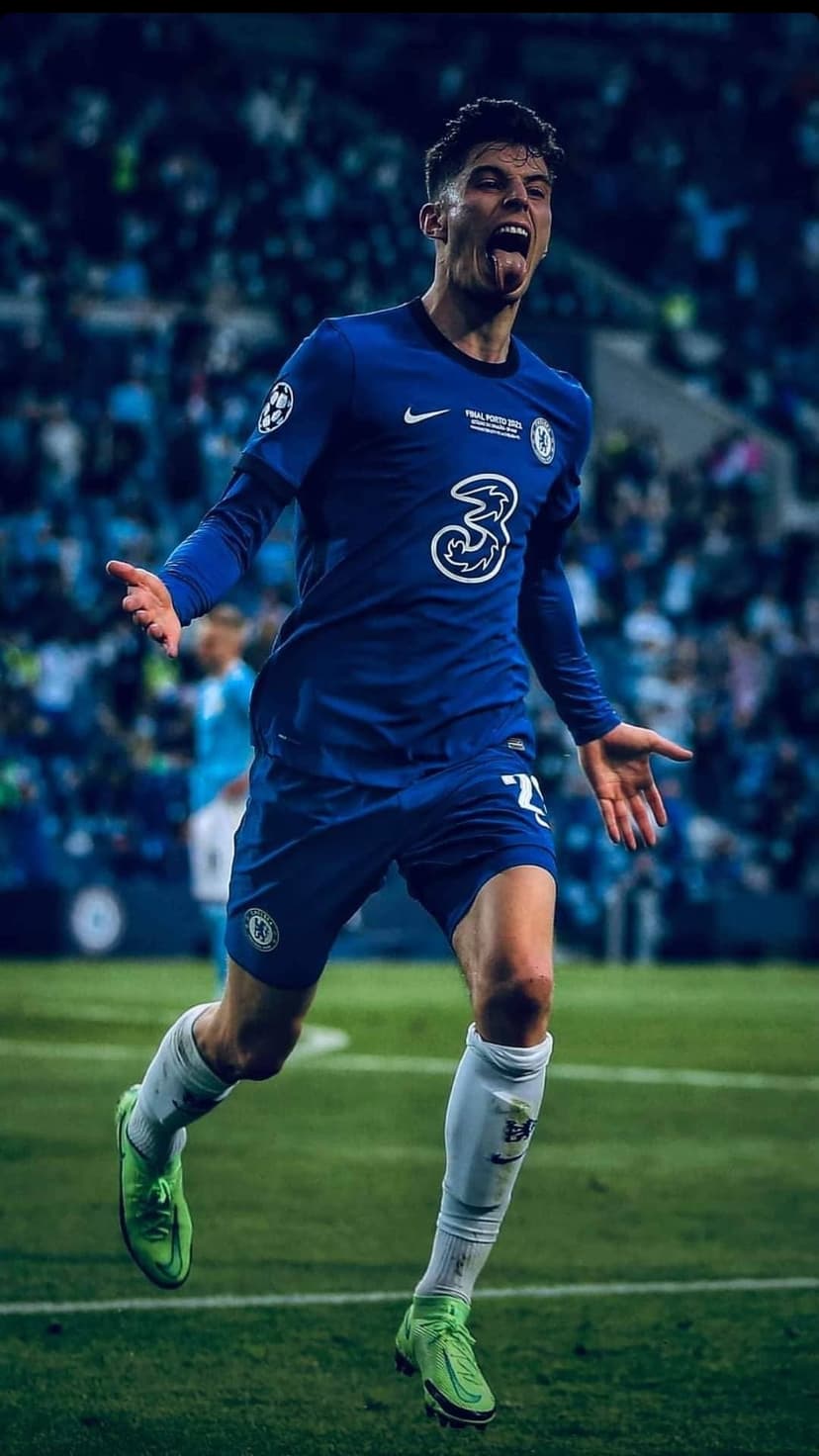 Kai Havertz celebrates a goal in a blue Chelsea jersey with arms out during a stadium football match.