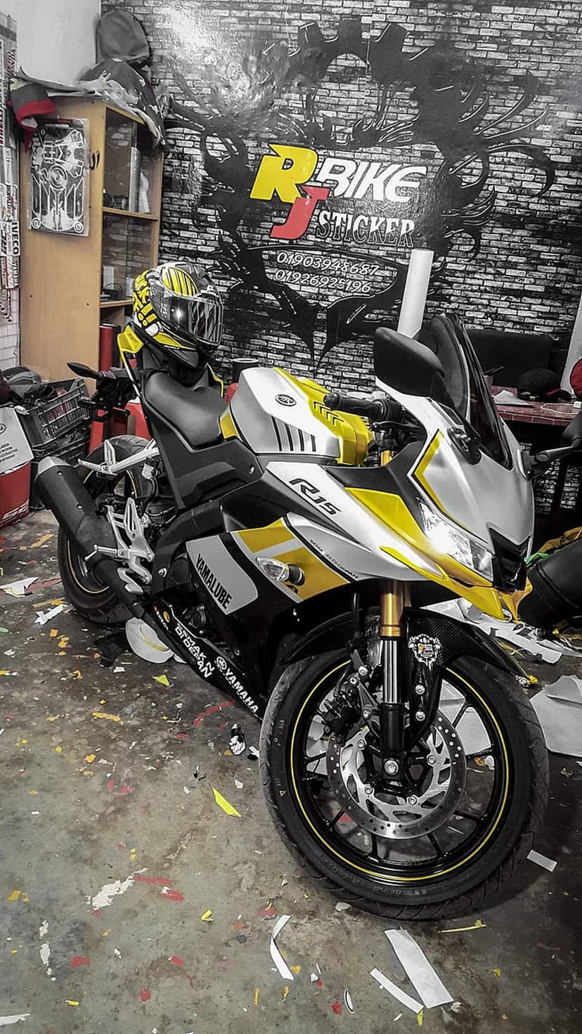Yamaha R15 motorcycle with yellow and silver decals parked in a workshop against a brick wall background.