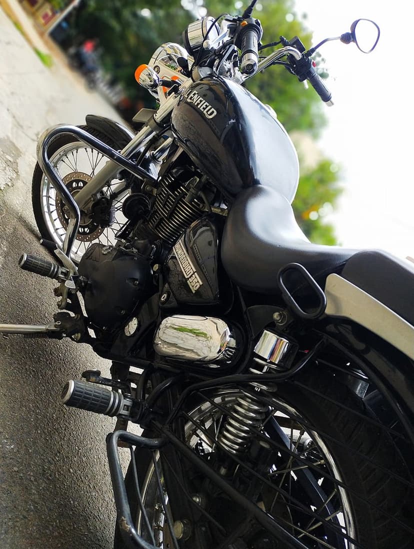 Black Royal Enfield motorcycle shows polished chrome handlebars and mirrors against a blurred outdoor background.