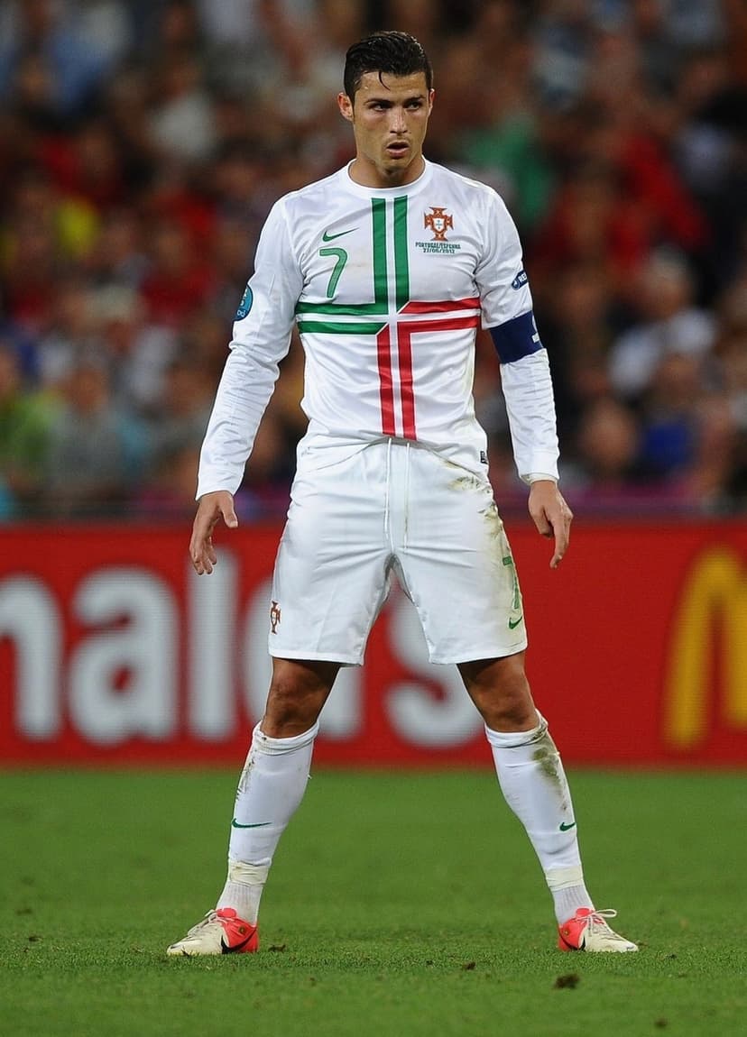 Cristiano Ronaldo in a white Portugal jersey with green accents stands on a football field during a match.