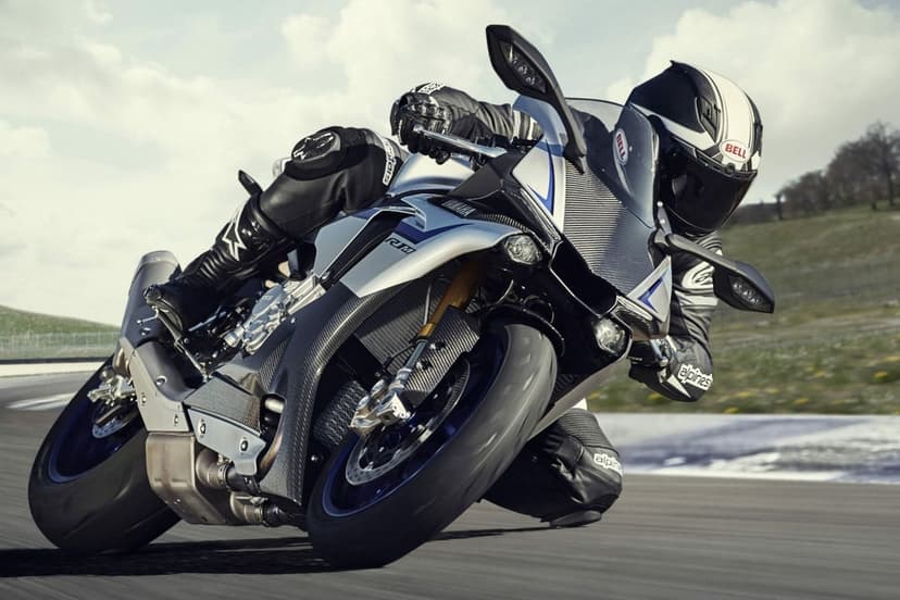 Motorcycle rider leaning a silver Yamaha sportbike into a sharp racetrack turn at high speed under a bright sky.