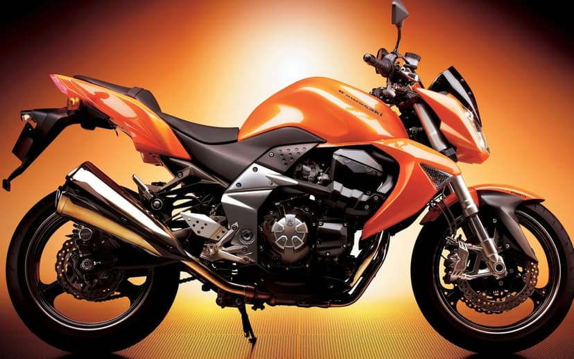 Orange Kawasaki sportbike in profile with metallic paint and chrome exhaust against a glowing orange background.