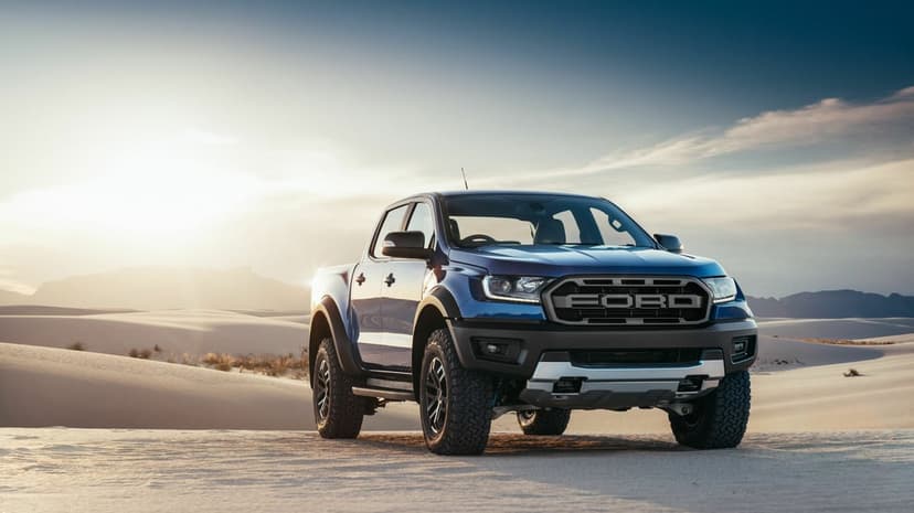 Blue Ford Ranger Raptor on white sand dunes at sunset with golden backlighting and soft mountain horizons.