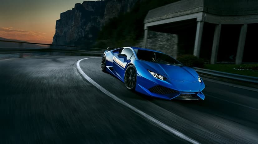 Blue supercar speeding through a curved mountain road at sunset with heavy motion blur and rugged cliffs.