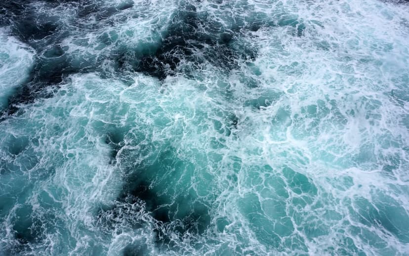 Turquoise ocean water and white sea foam swirls create a turbulent, top-down view of churning deep sea currents.