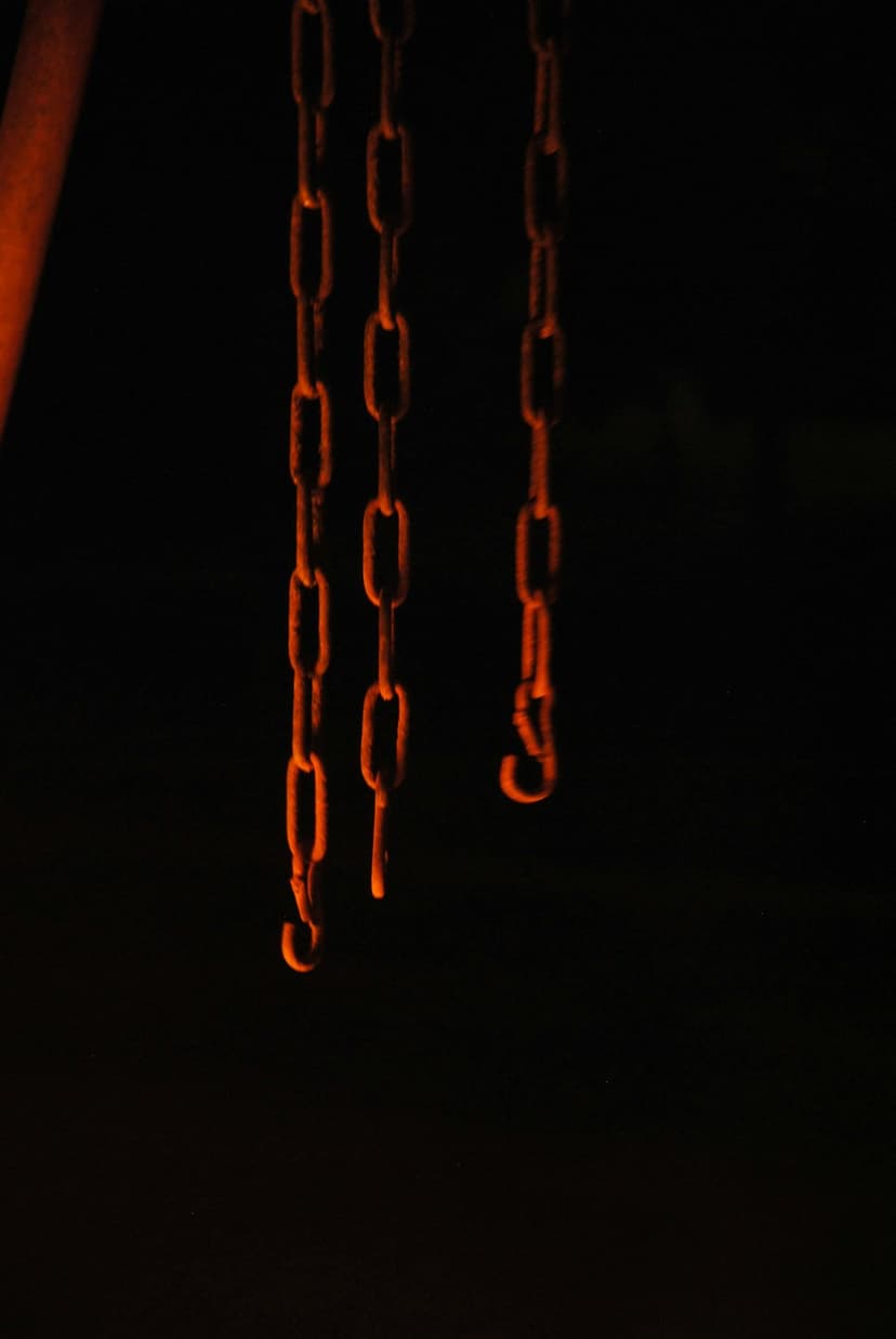 Three metallic chains illuminated with orange light against a solid black background show detailed iron links.