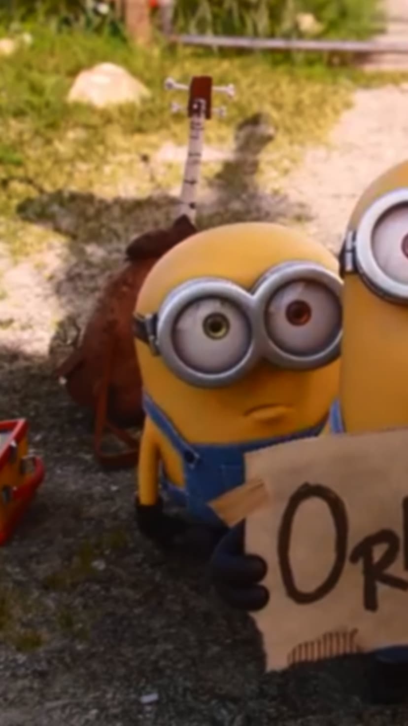 Sad yellow minion holds a For Rent cardboard sign on grass next to a red ukulele and brown backpack.