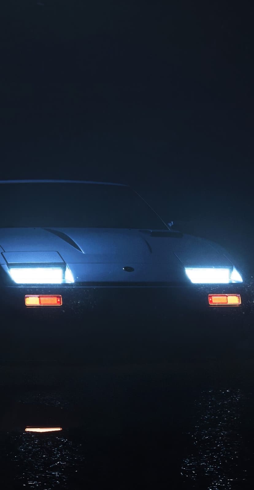 Retro pop-up car headlights and amber side lights illuminate a foggy night scene with wet ground reflections.
