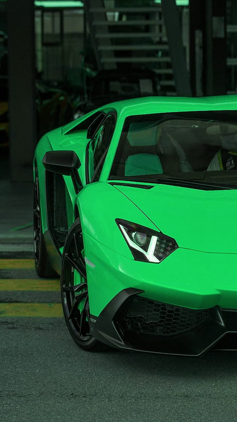 Bright green Lamborghini Aventador front headlight and grille detail on asphalt with yellow racing lines.