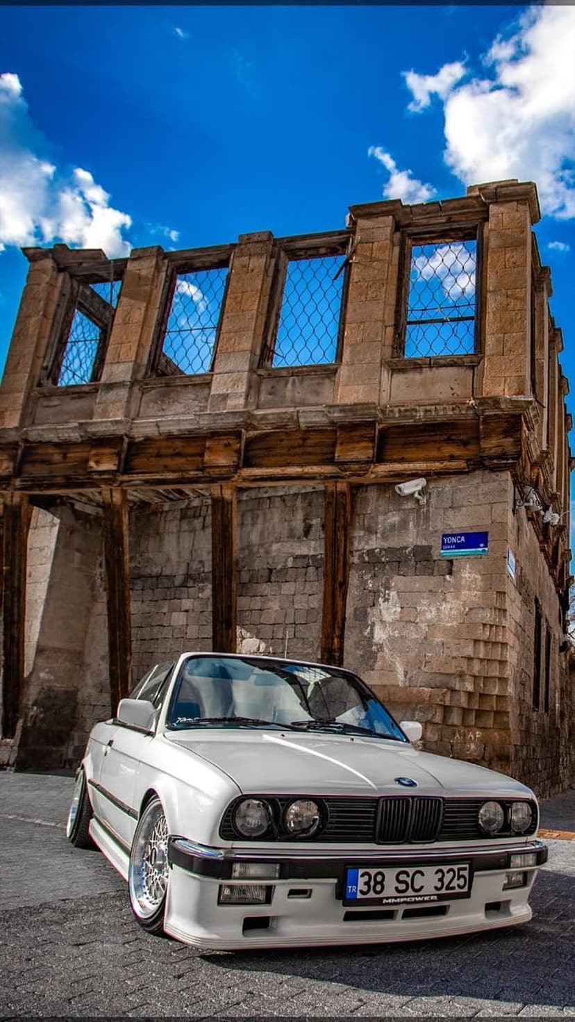 White vintage BMW convertible parked near a weathered stone building with empty window frames and a blue sky.
