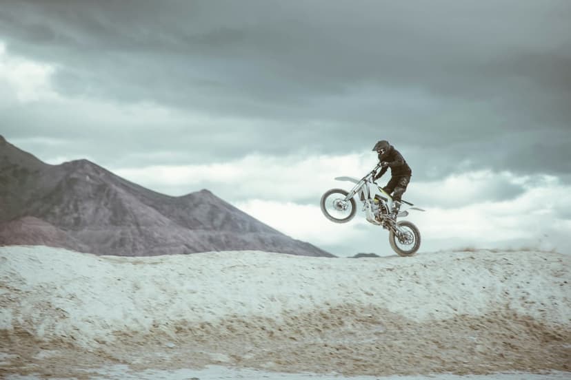 Motocross athlete performs a high jump on a dirt bike over a dusty ridge against a brooding stormy sky.