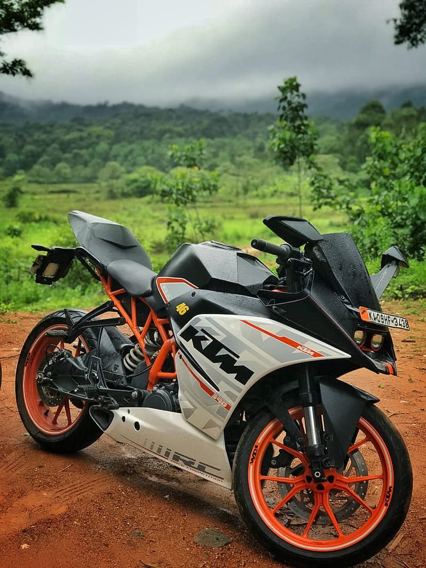 KTM RC motorcycle with orange wheels parked on a dirt road facing misty green mountains under a cloudy sky.