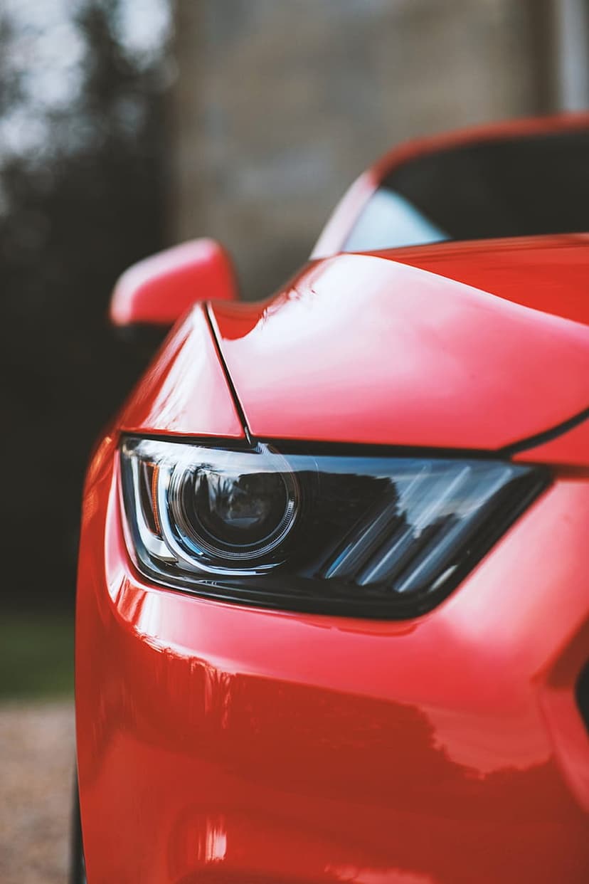 Red Ford Mustang headlight with sharp LED internals and glossy crimson paint reflecting the surrounding environment.