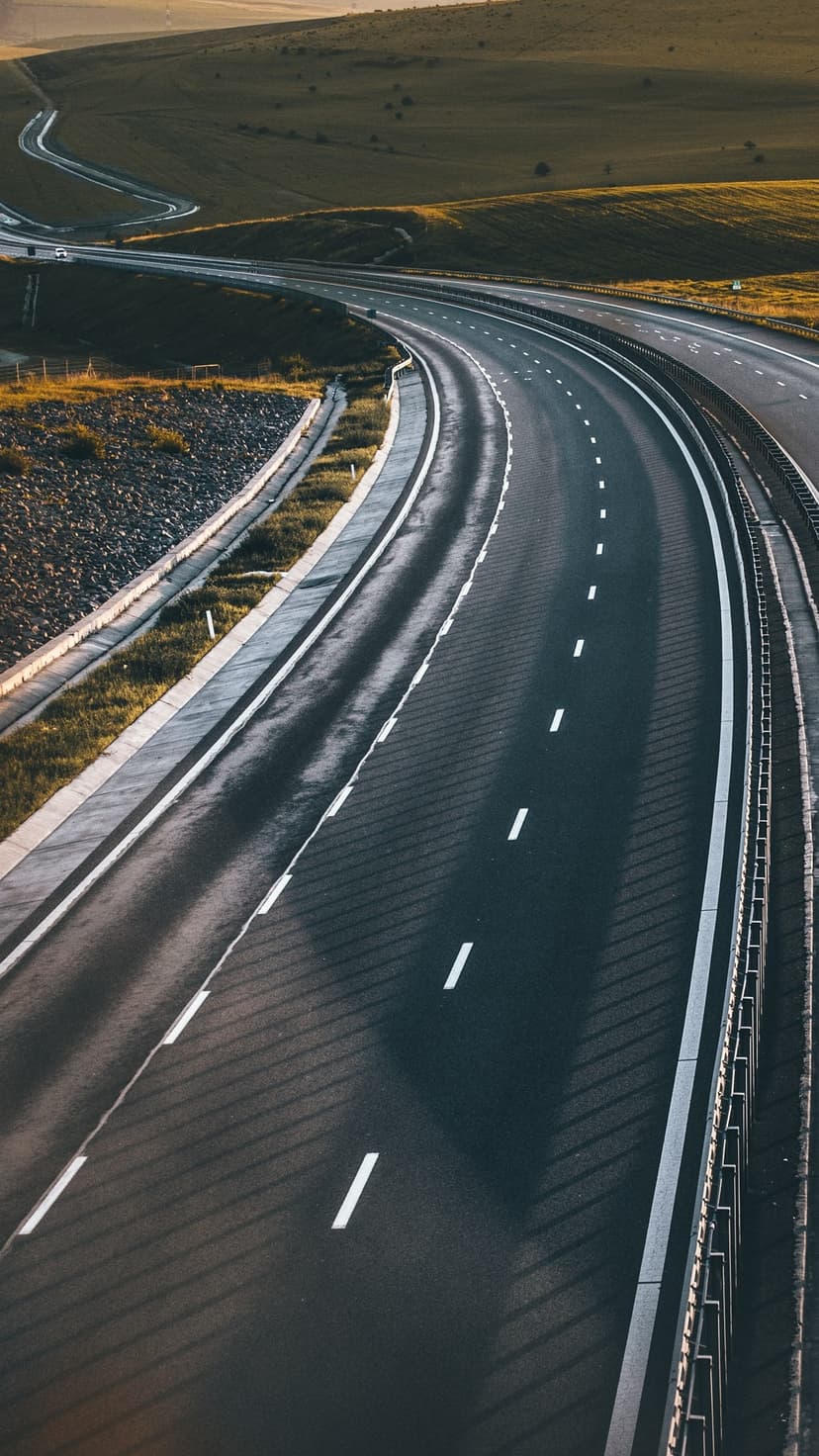 Multi-lane asphalt highway curves through rolling green hills and rural fields under soft morning light.