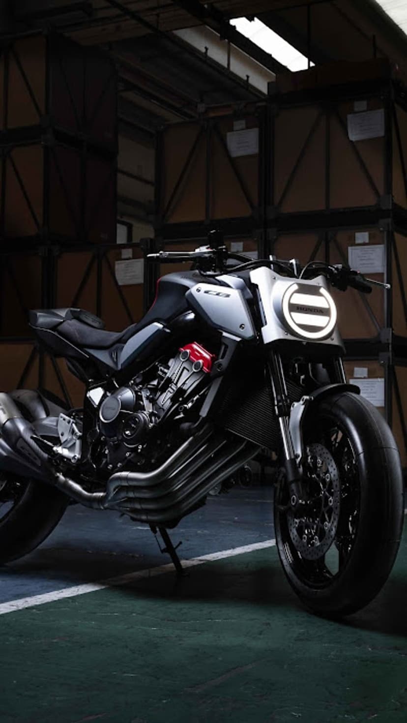 Honda motorcycle with circular LED headlight and red engine accents parked in a dim industrial warehouse.
