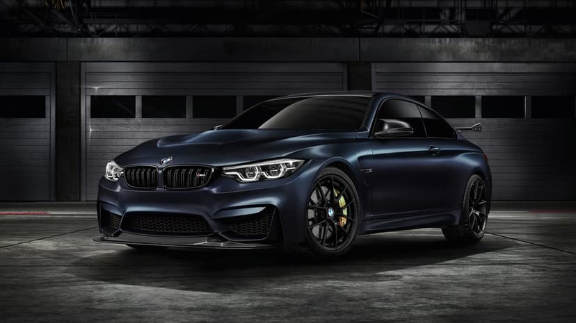 Matte navy BMW M4 GTS sports car in a dark industrial garage with dramatic lighting and gold brake calipers.